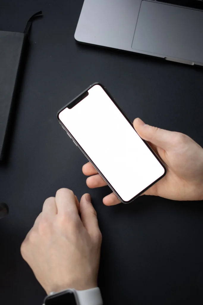 Hand houdt een smartphone met blanco scherm vast naast een laptop