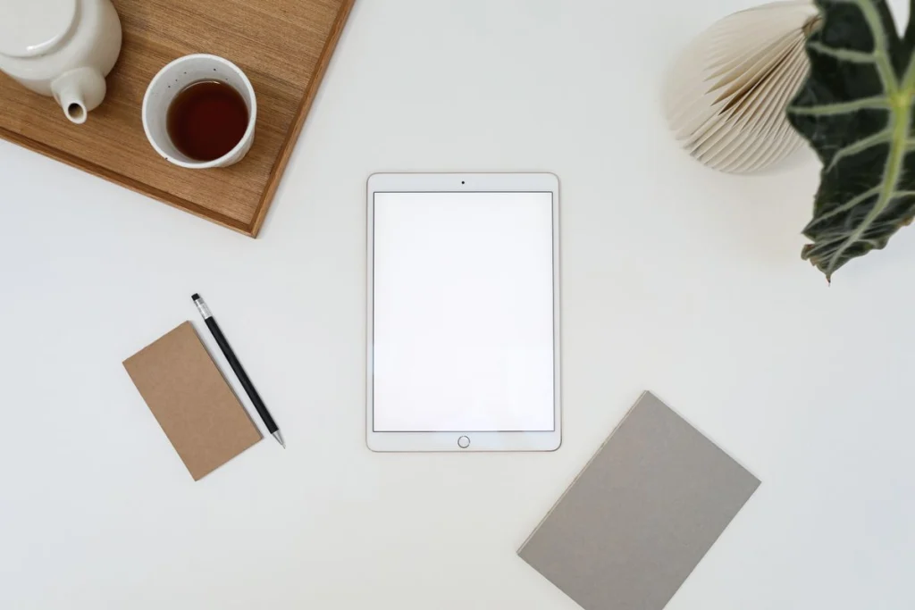 Tablet met leeg scherm op een licht bureau naast thee en notitieboek